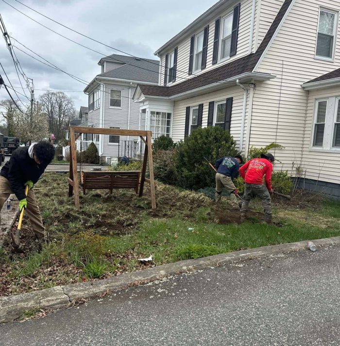 Workers renovating a small front yard with budget landscaping makeover in front of a residential home