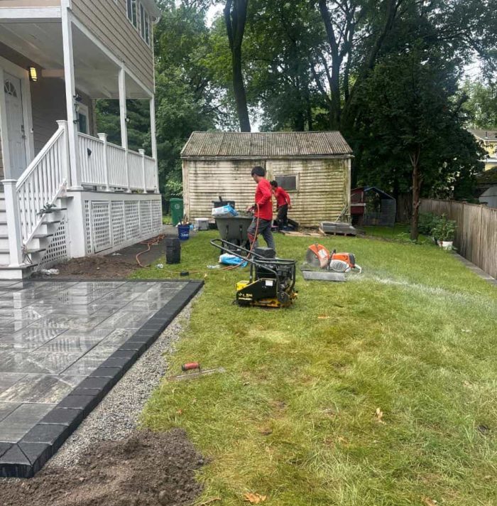 Landscaping around a paver patio with new lawn edges and prepared soil beside a home