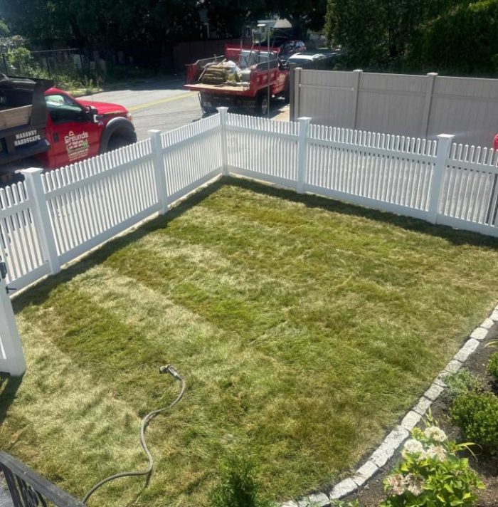Lawn edging around a white vinyl fence with a defined grass area and landscaped planting bed by Grounds of Nature Landscaping And Tree Services